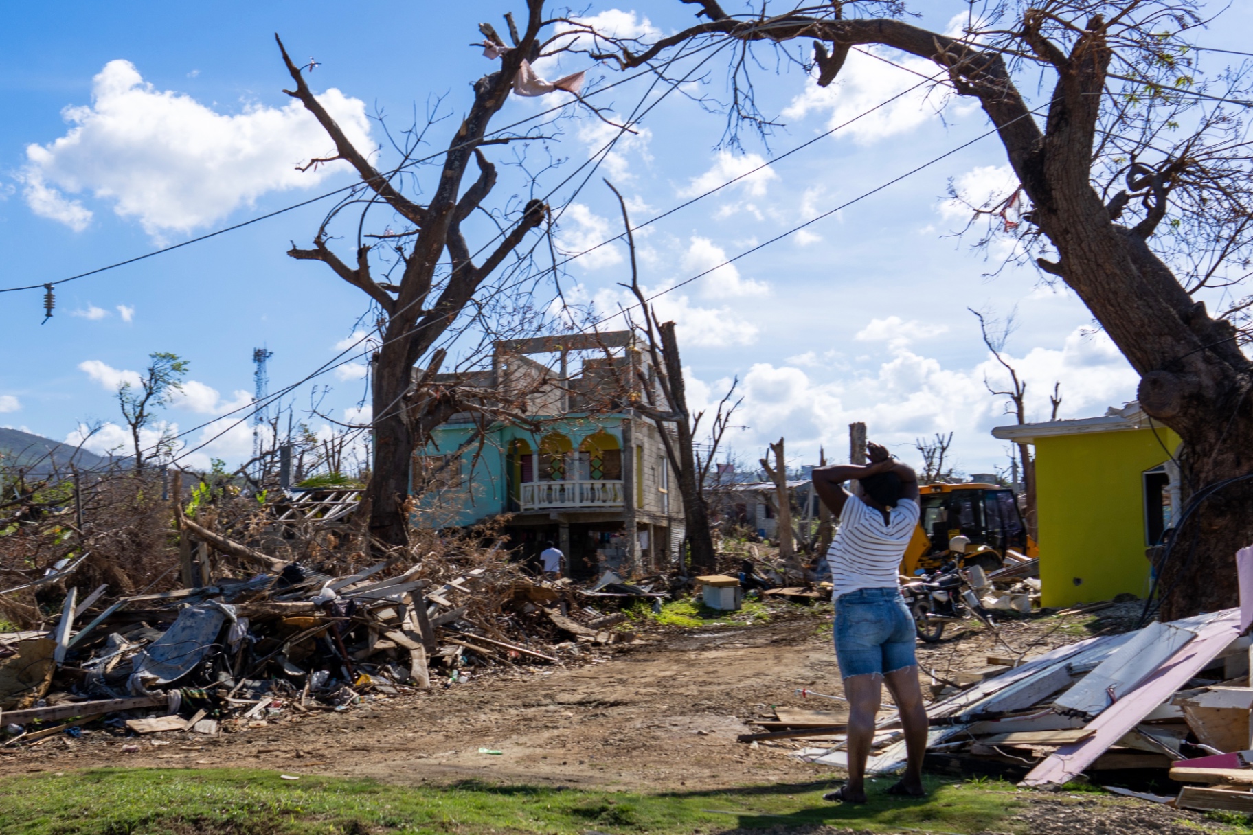 Woman standing among debris and damaged homes after Hurricane Melissa in St Elizabeth, Jamaica