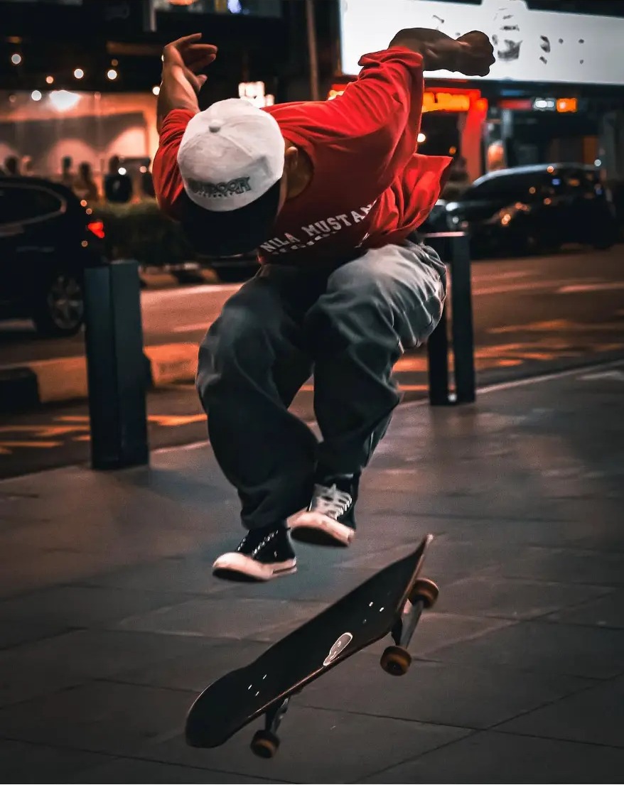 Skateboarder mid-trick on a city pavement at night