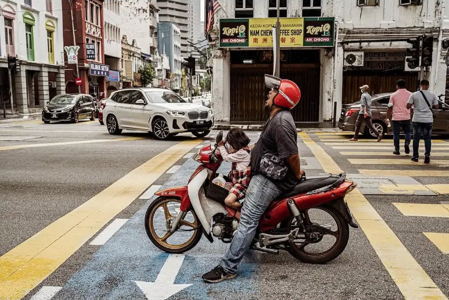 A father and daughter waiting on a motorbike at a crossing