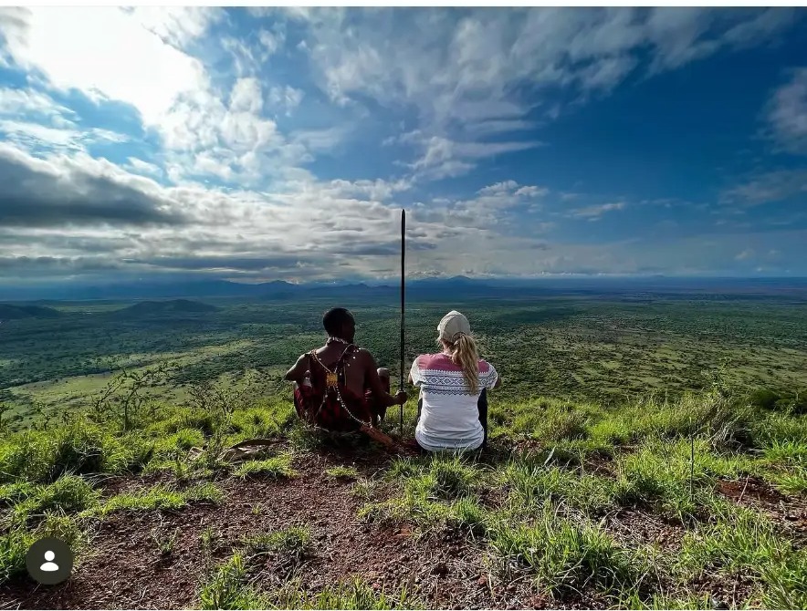 Masai guide and visitor looking out over the green plains from a hilltop in Tsavo West, Kenya