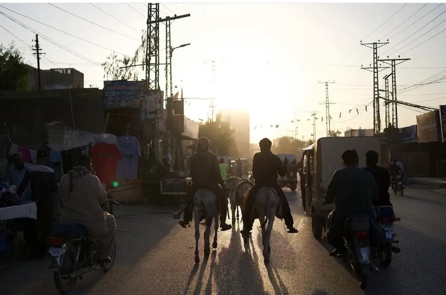 Donkey riders and motorbikes heading into the low sun on a road in Sukkur, Sindh, Pakistan