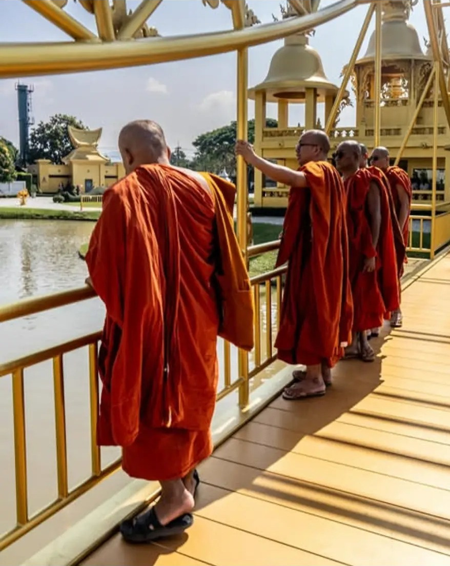 Monks in orange robes crossing the golden bridge at Wat Rong Khun, Chiang Rai, Thailand