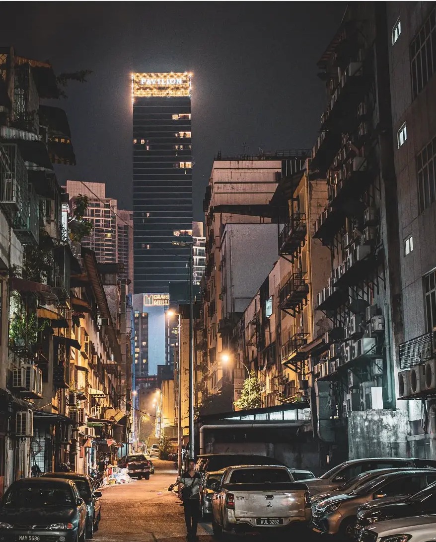 Man walking up a narrow street at night with the Pavilion tower lit above