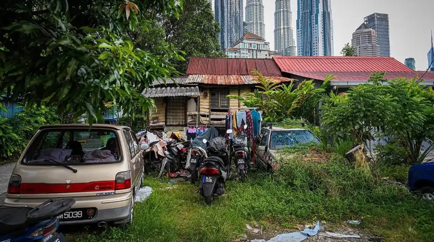 Traditional wooden village houses and parked scooters with the Petronas Towers rising behind