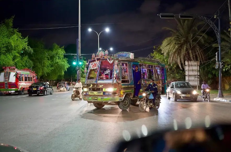 Brightly decorated bus and motorbikes at a wet crossroads at night in Karachi, Pakistan