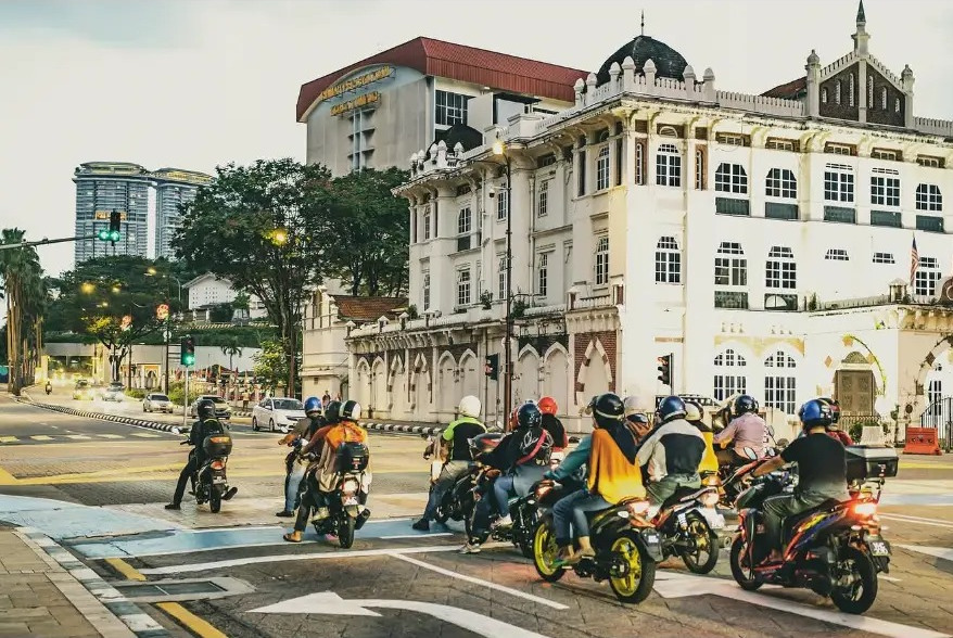 Motorbike riders waiting at a crossing in front of colonial architecture