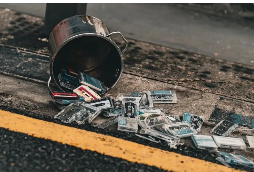 Tipped-over metal bucket spilling old cassette tapes across the kerb