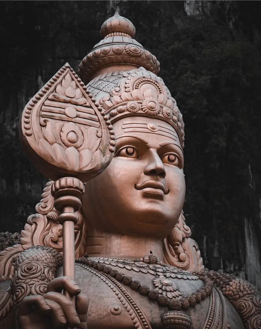 The golden Arulmigu Murugan statue against the limestone cliffs