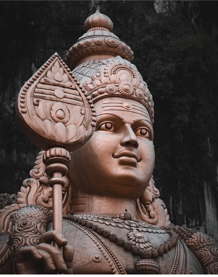 The golden Arulmigu Murugan statue against the limestone cliffs
