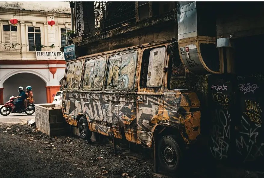 Rusted van covered in graffiti beside a shophouse