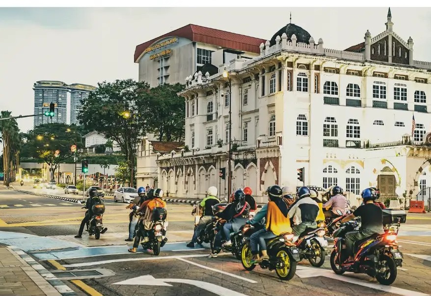 Motorbike riders waiting at a crossing in front of colonial architecture