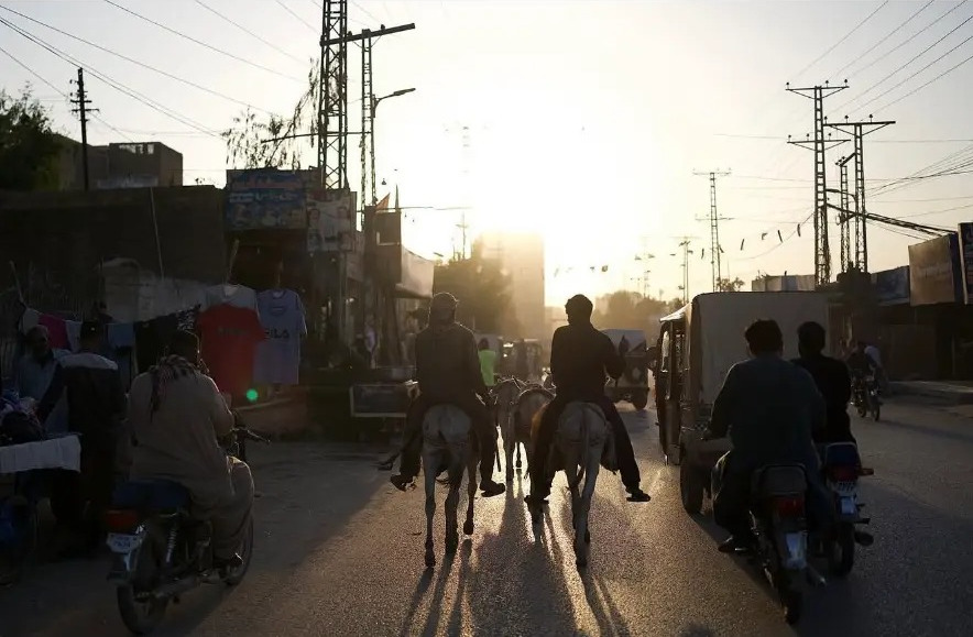 Donkey riders and motorbikes heading into the low sun on a road in Sukkur, Sindh, Pakistan