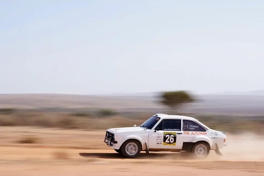 White rally car number 26 sliding through desert dust