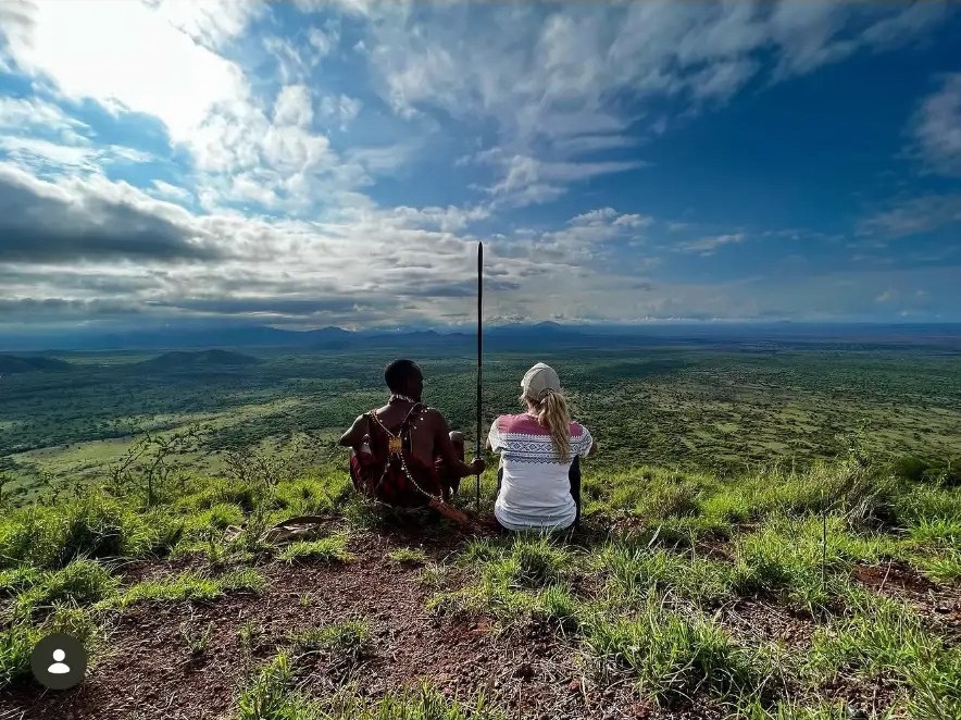 Masai guide and visitor looking out over the green plains from a hilltop in Tsavo West, Kenya