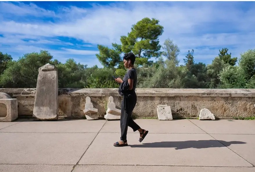 Woman walking past ancient stone fragments below the Acropolis, Athens, Greece