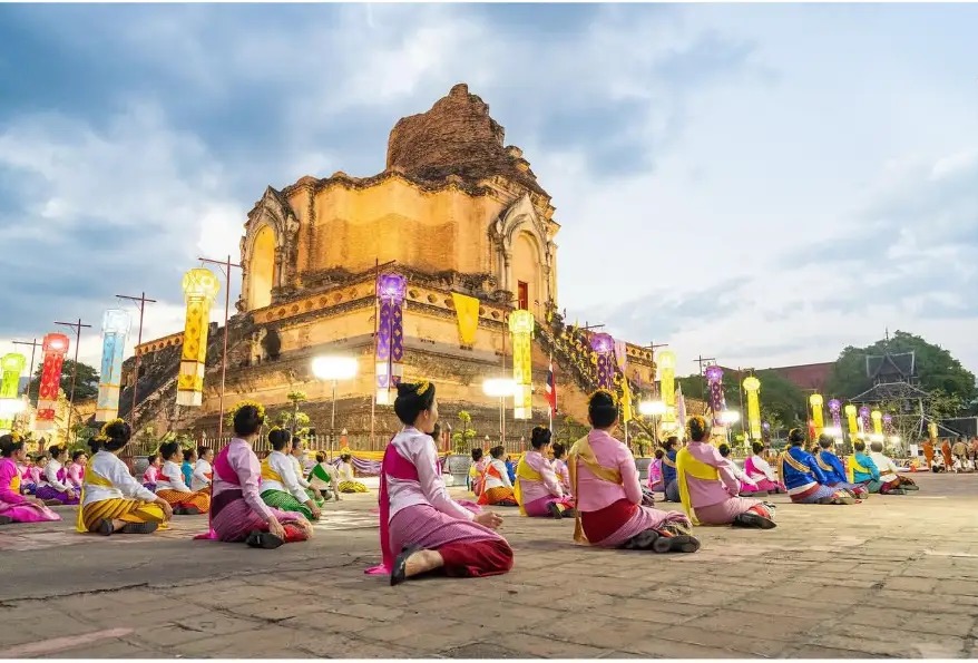 Dancers in traditional dress kneeling before Wat Chedi Luang at dusk in Chiang Mai, Thailand