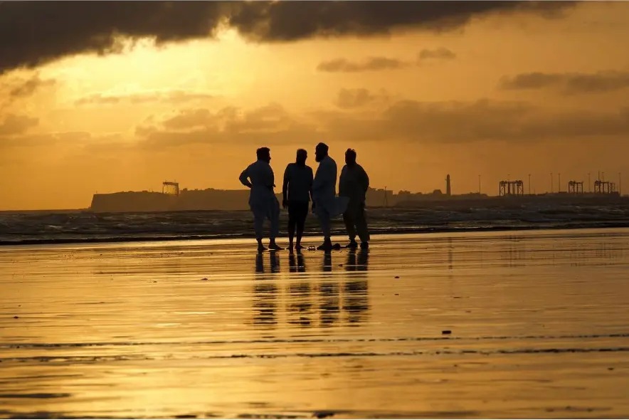 Four men talking in silhouette on a golden, mirror-like beach at sunset in Karachi, Pakistan