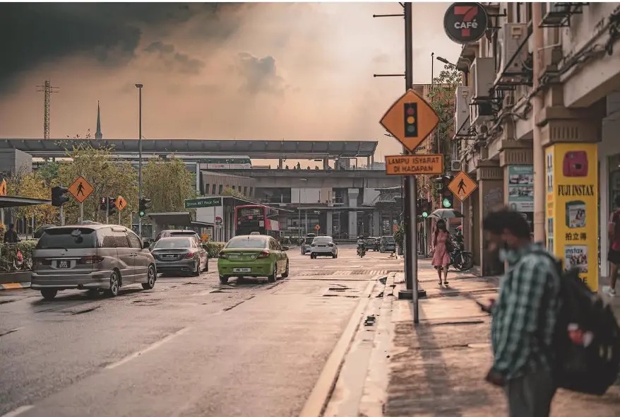 Wet street with traffic signs and passers-by under a sunset sky