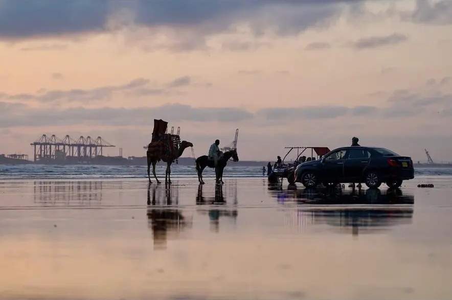 Camel and horse riders reflected on the wet sand at sunset on Sea View Beach, Karachi, Pakistan