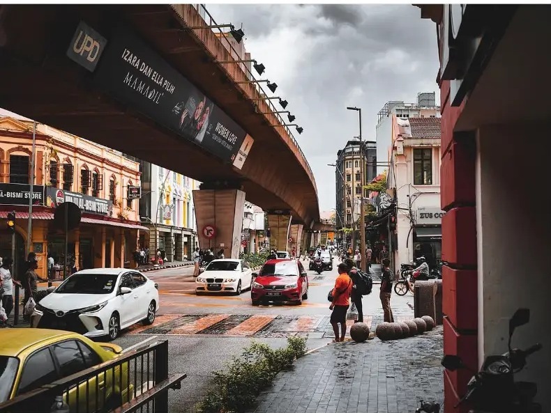 Busy street under a curving flyover with traffic and pedestrians in Kuala Lumpur, Malaysia