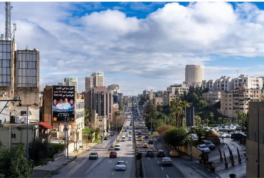 Traffic flowing down a wide boulevard between hillside buildings in Amman, Jordan
