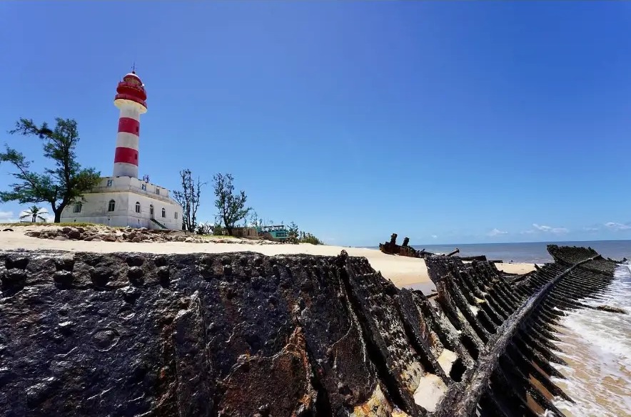 Red and white lighthouse behind the rusted wreck of a ship on the beach