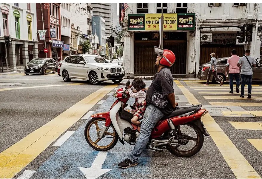 A father and daughter waiting on a motorbike at a crossing