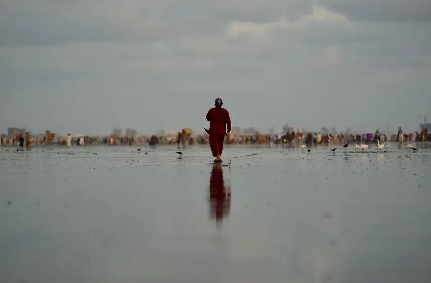 Man in a red shalwar kameez walking on the mirror-like beach in Karachi, Pakistan