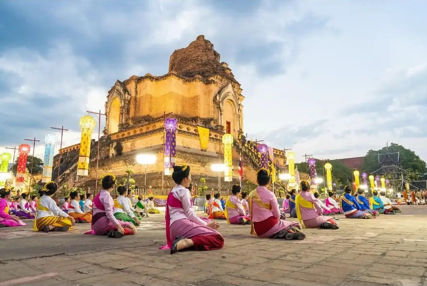 Dancers in traditional dress kneeling before Wat Chedi Luang at dusk in Chiang Mai, Thailand