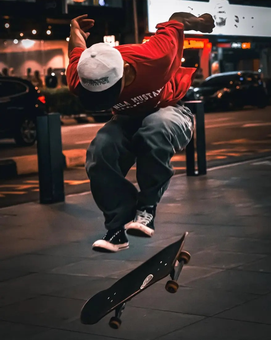 Skateboarder mid-trick on a city pavement at night