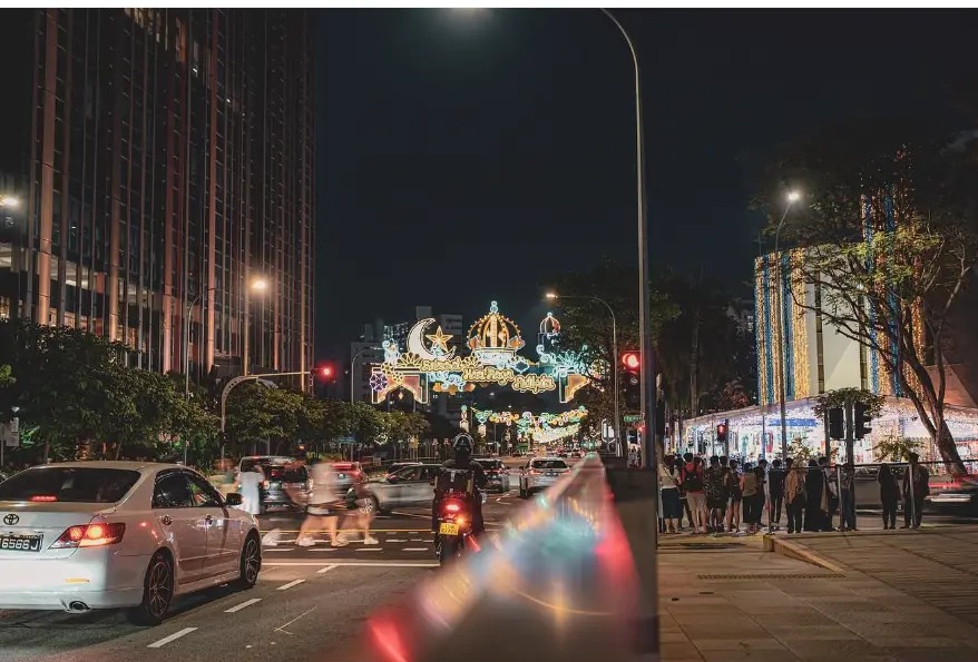 Street decorated with festive lights at night with passing traffic