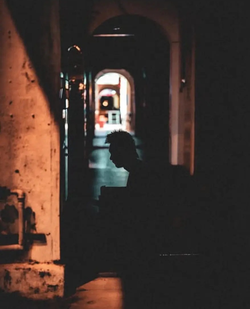 Silhouette of a man in a dark alley lit by warm shopfront light