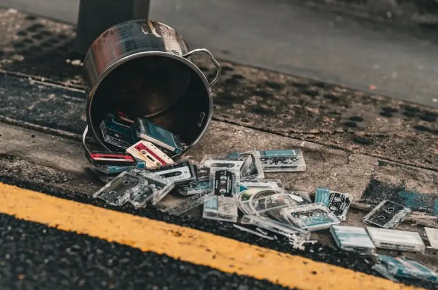 Tipped-over metal bucket spilling old cassette tapes across the kerb
