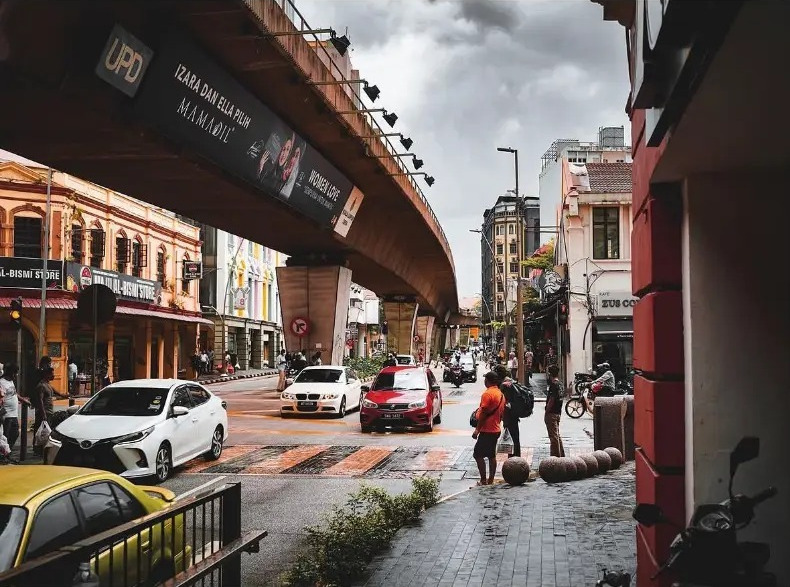 Busy street under a curving flyover with traffic and pedestrians in Kuala Lumpur, Malaysia