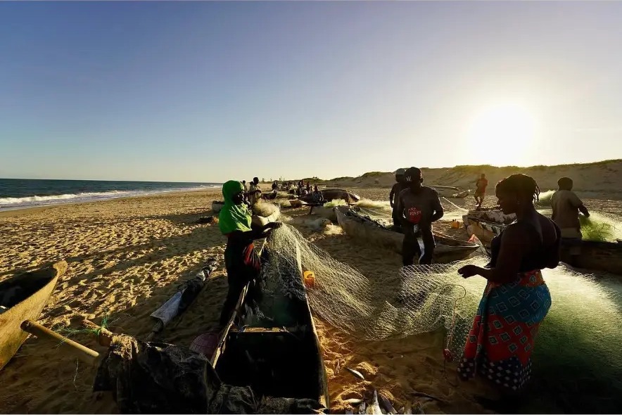 Fishermen and women hauling nets beside dugout canoes at sunrise