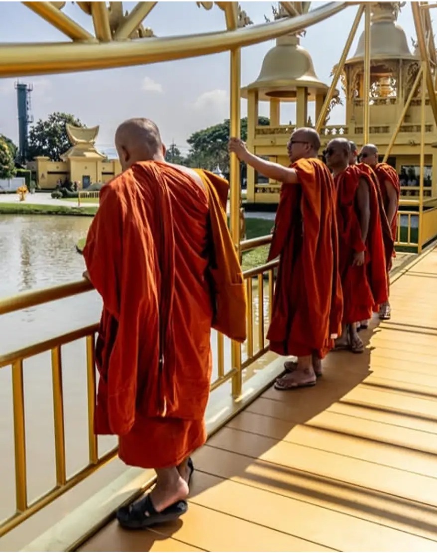Monks in orange robes crossing the golden bridge at Wat Rong Khun, Chiang Rai, Thailand