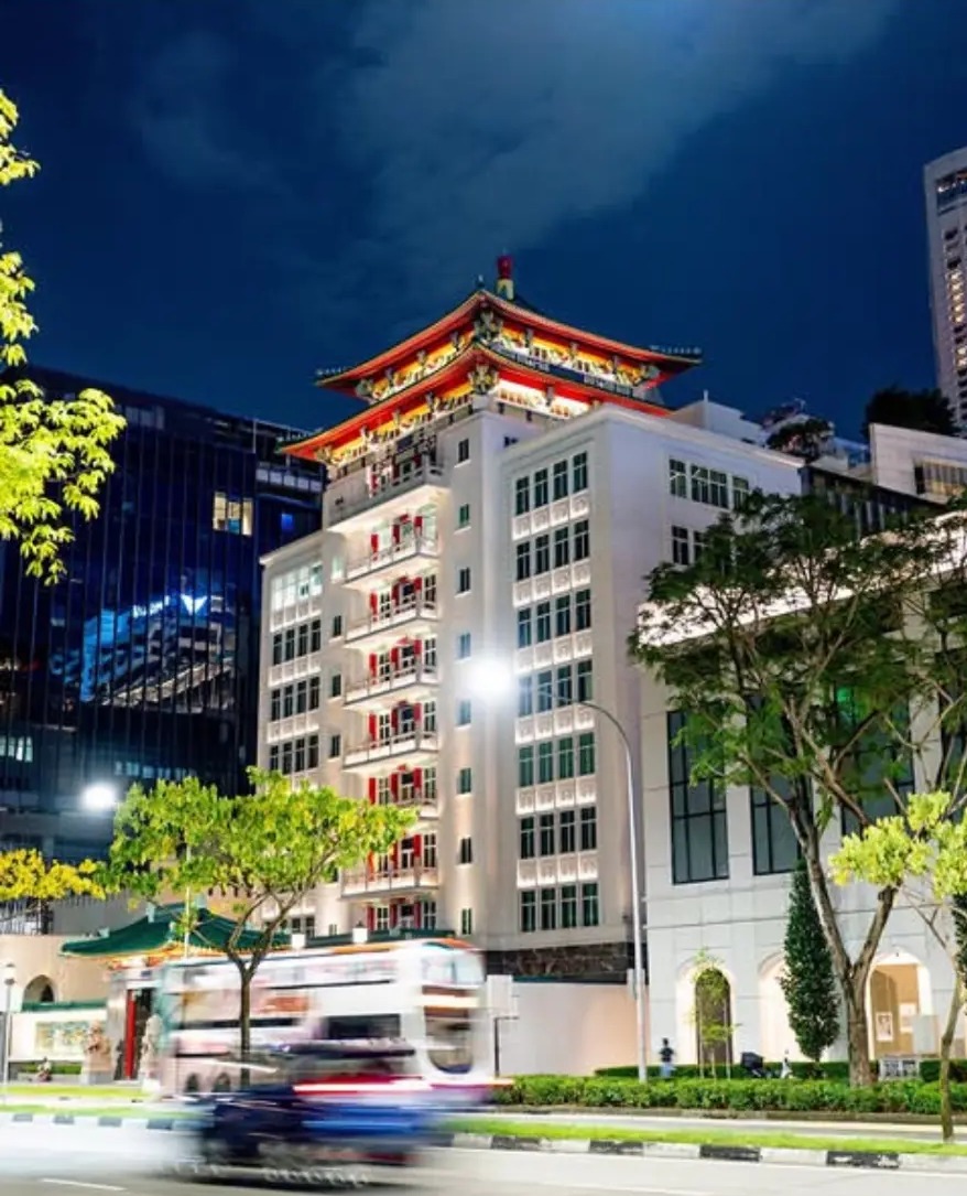 Colonial building with a pagoda roof lit at night as a bus blurs past