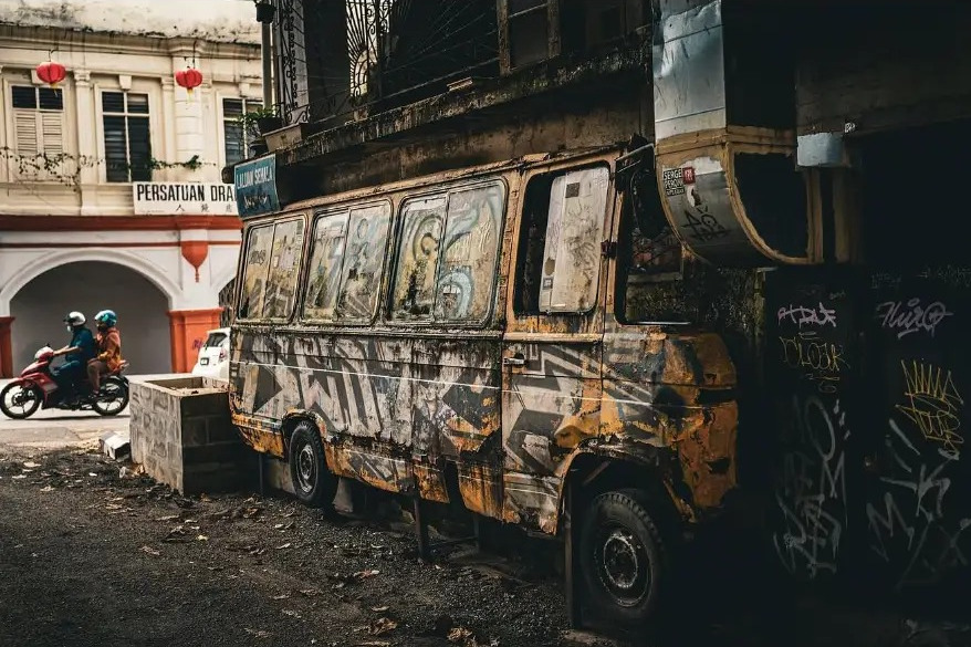 Rusted van covered in graffiti beside a shophouse