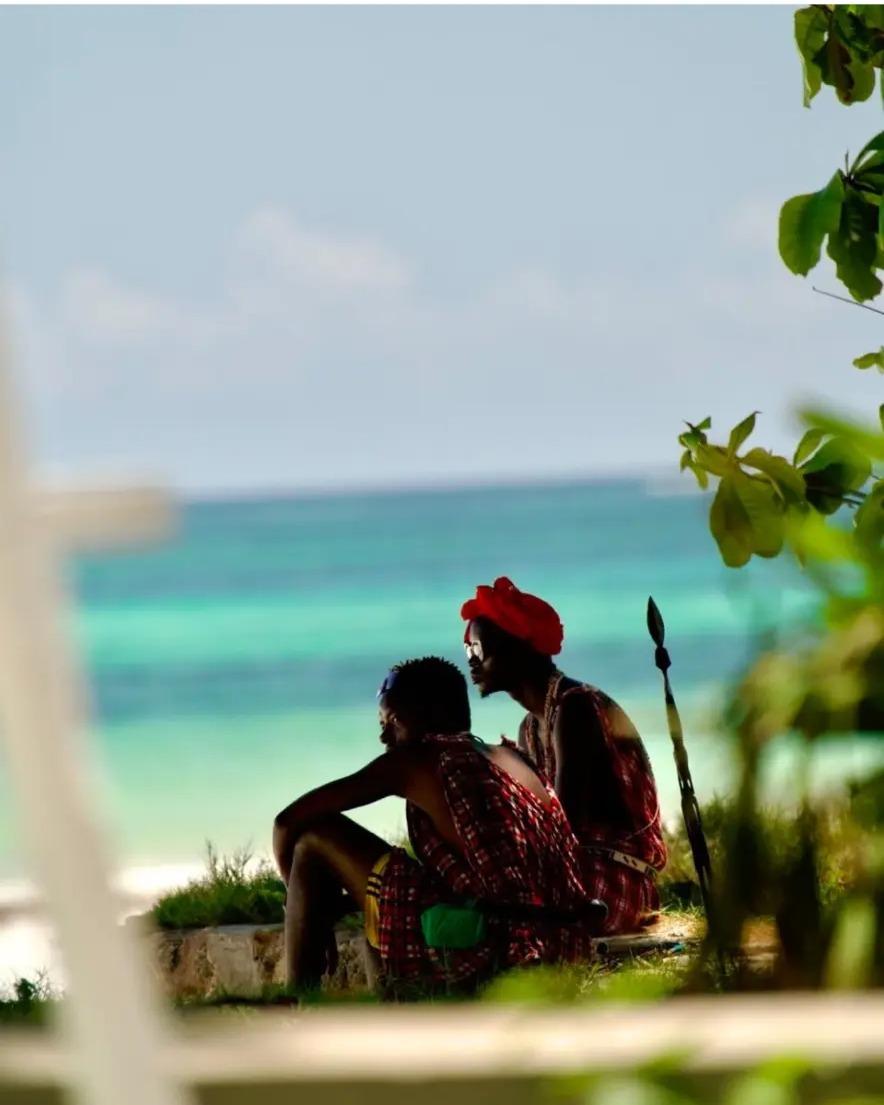 Two Masai men in red shukas sitting above the turquoise water at Diani Beach, Kenya