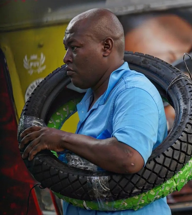 Man carrying a motorbike tyre over his shoulder on Tom Mboya Street in Nairobi, Kenya